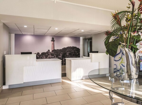 Un área de recepción con diseño moderno, que incluye un mostrador de recepción, una mesa de vidrio y una planta decorativa.