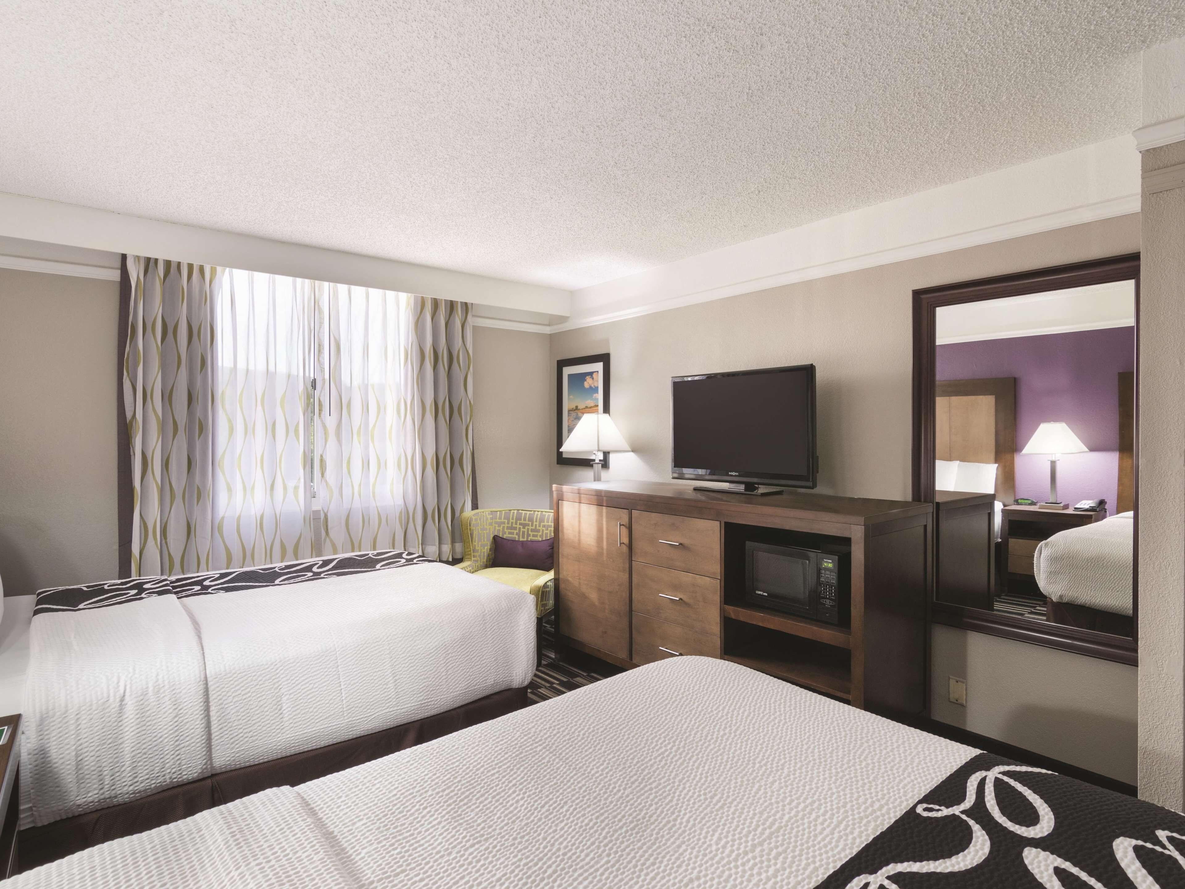 A hotel room with two beds, a television, a desk with a lamp, and a mirror.