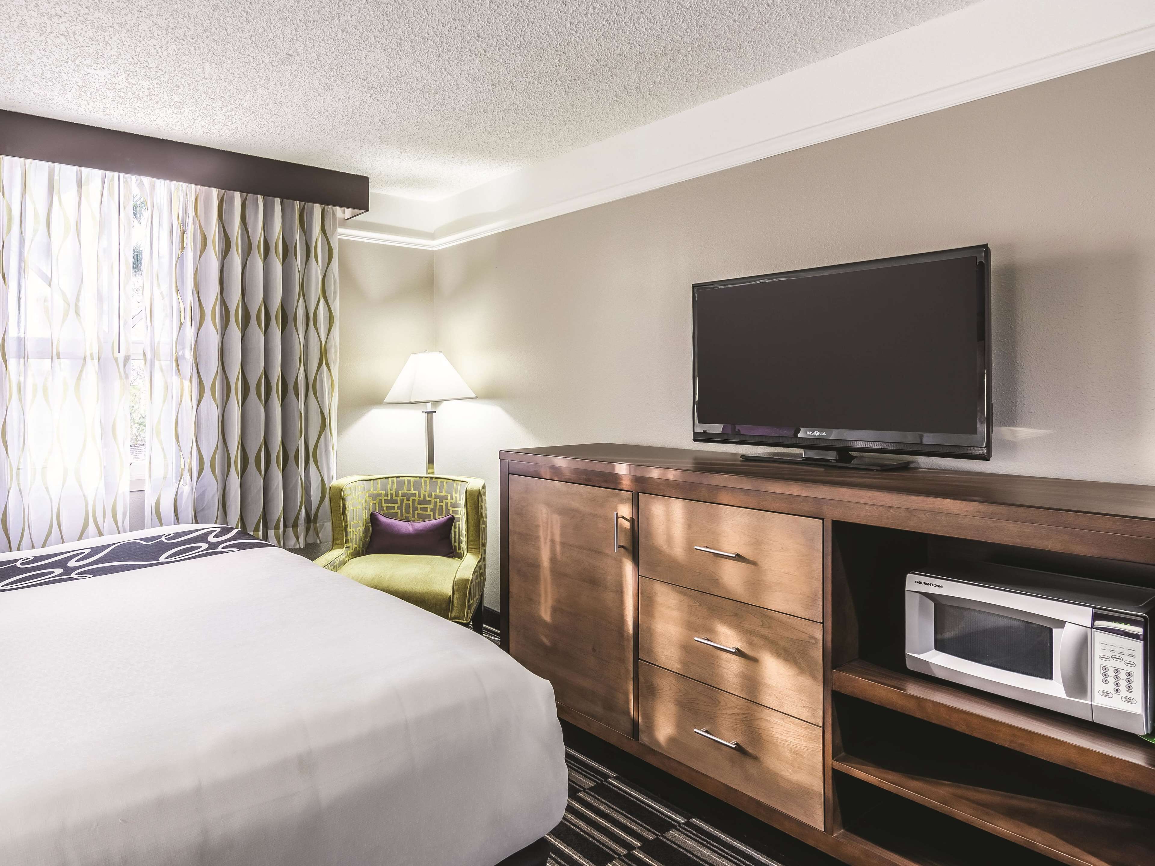 A hotel room with a bed, a television on a wooden cabinet, a microwave, and a lamp.
