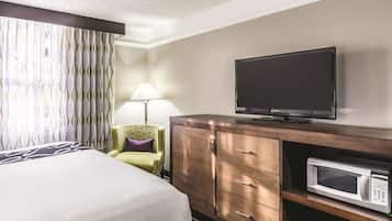 A hotel room with a bed, a television on a wooden cabinet, a microwave, and a lamp.