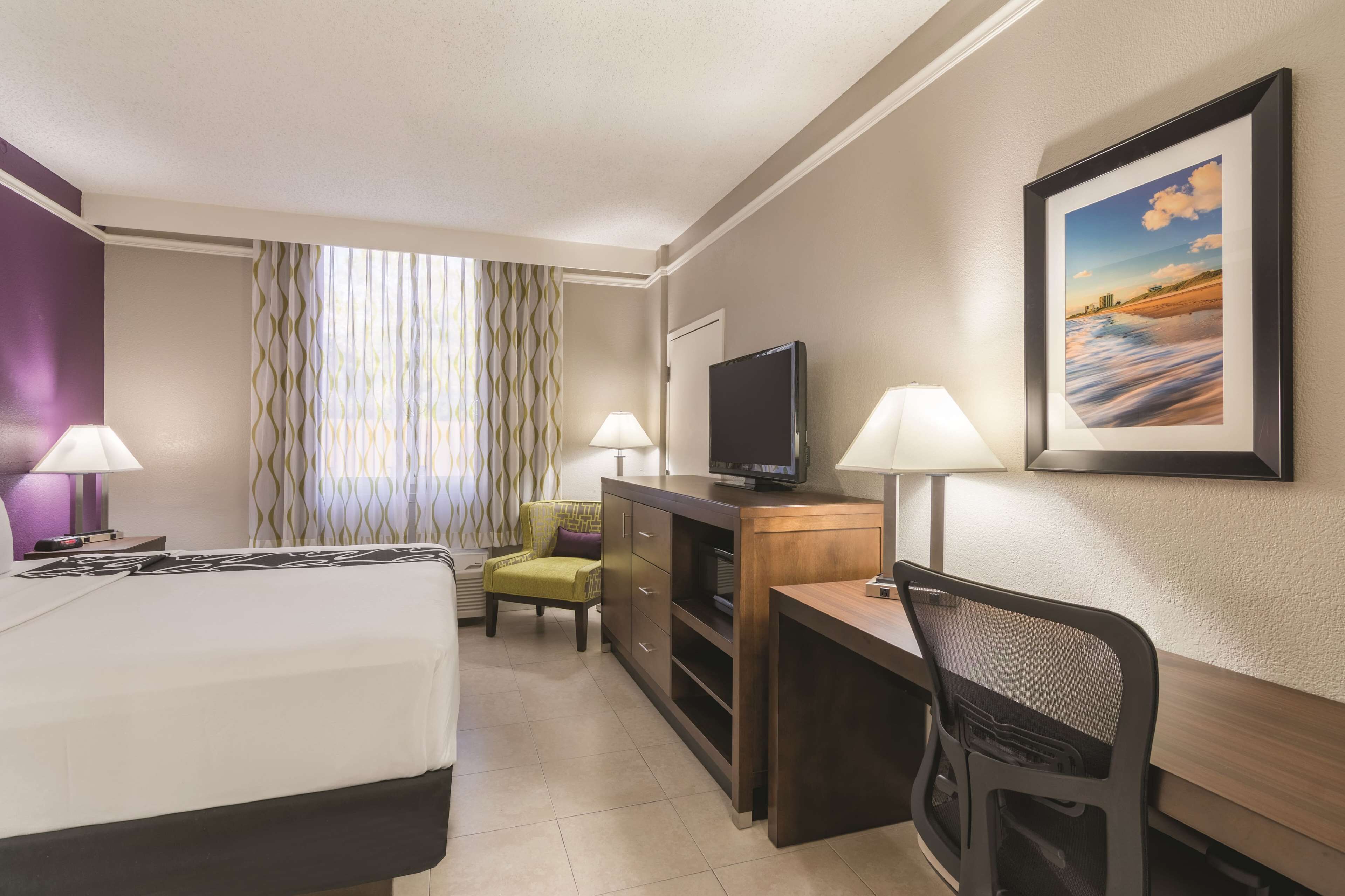 A hotel room with a bed, a desk, a chair, a television, and two lamps.