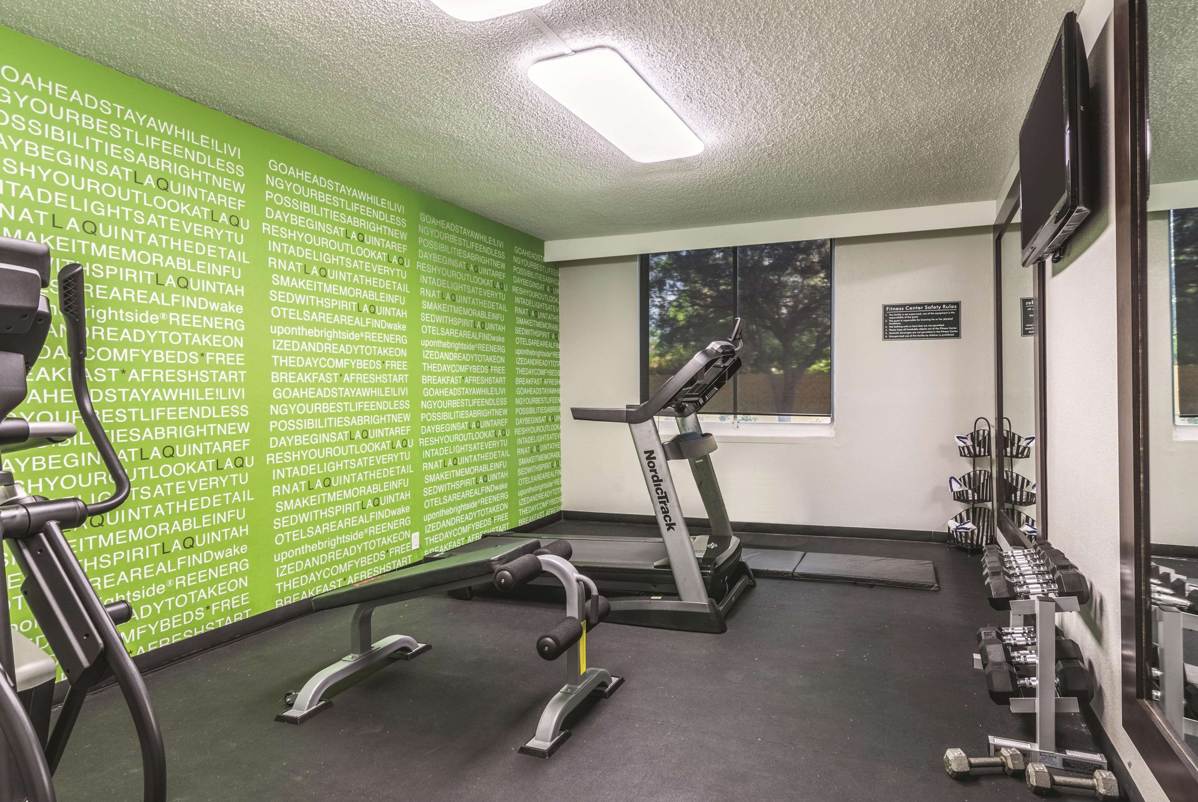 Une salle de sport équipée de matériel d’exercice, d’un tapis de course et d’un mur orné de messages motivants.
