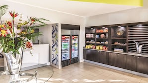 A reception area with a glass table, a vase of flowers, a Coca-Cola refrigerator, snack shelves, and a decorative bowl.