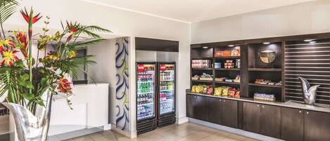 A reception area with a glass table, a vase of flowers, a Coca-Cola refrigerator, snack shelves, and a decorative bowl.
