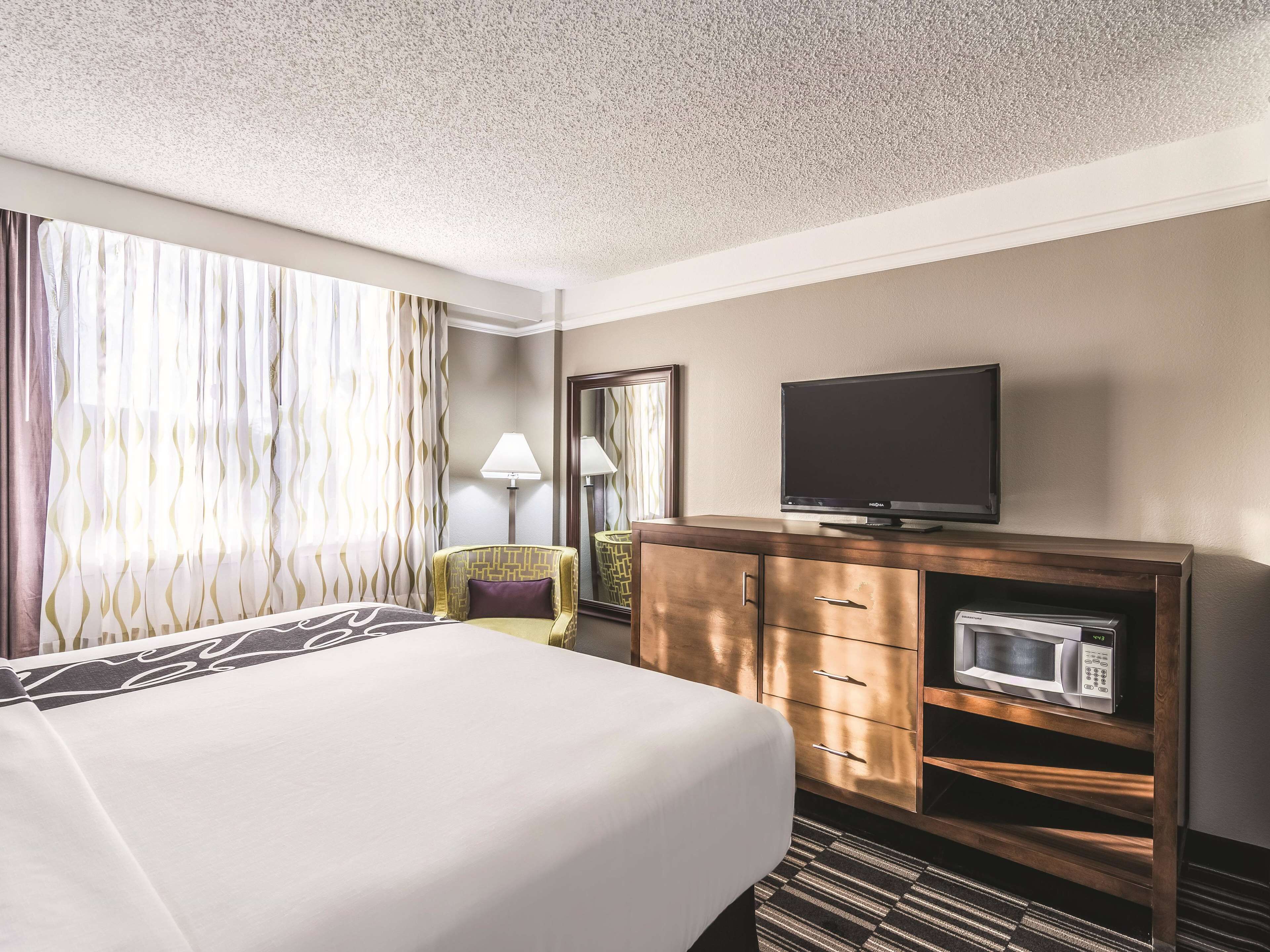 A hotel room with a bed, a television on a wooden cabinet, a microwave, and a lamp.