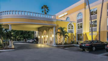 A hotel entrance with a curved balcony, palm trees, and a parking lot.
