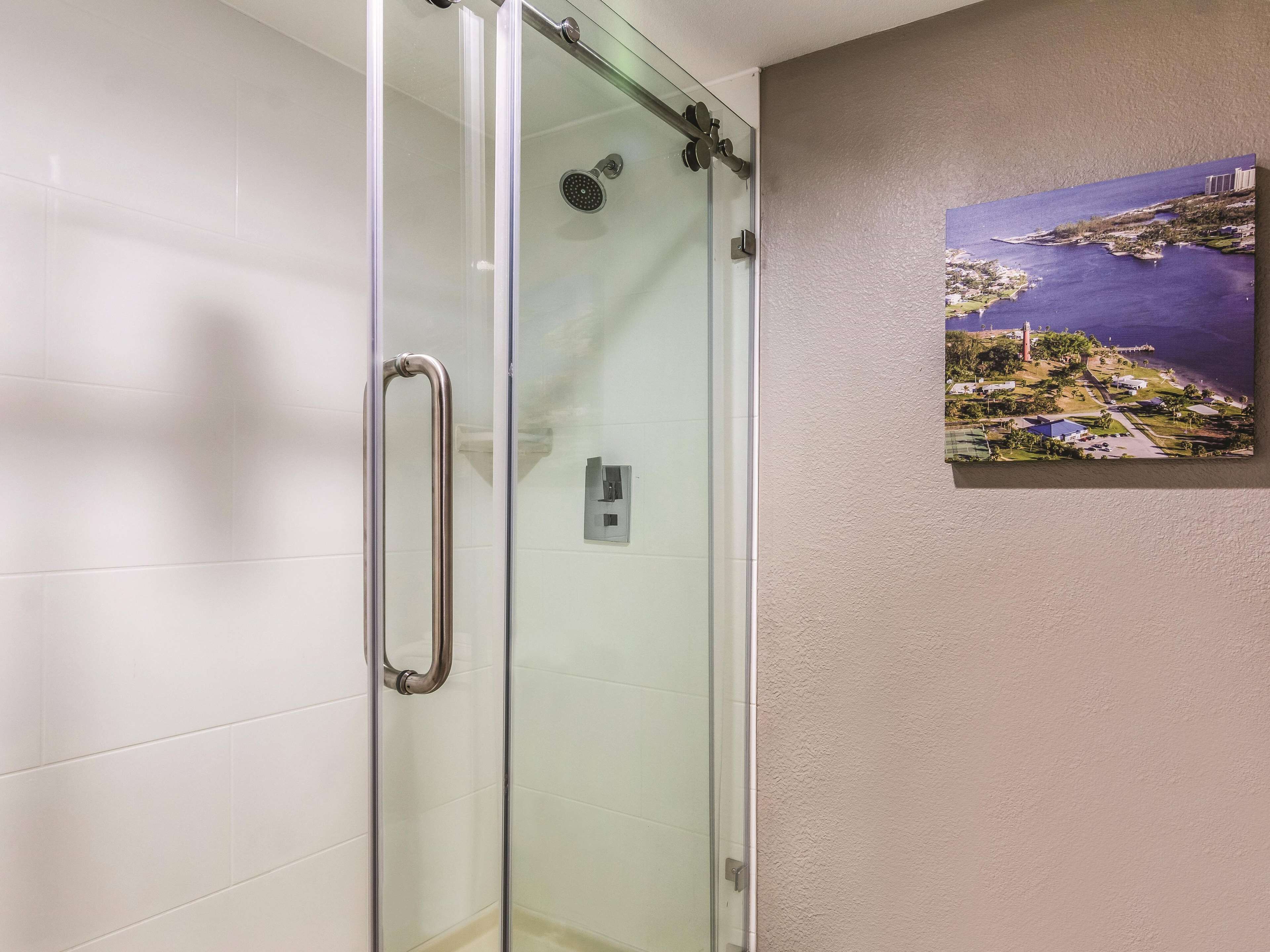 Eine gläserne Dusche mit Handlauf, einem an der Wand montierten Lichtschalter und einem gerahmten Gemälde von Küstenlandschaft.