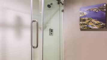 Eine gläserne Dusche mit Handlauf, einem an der Wand montierten Lichtschalter und einem gerahmten Gemälde von Küstenlandschaft.