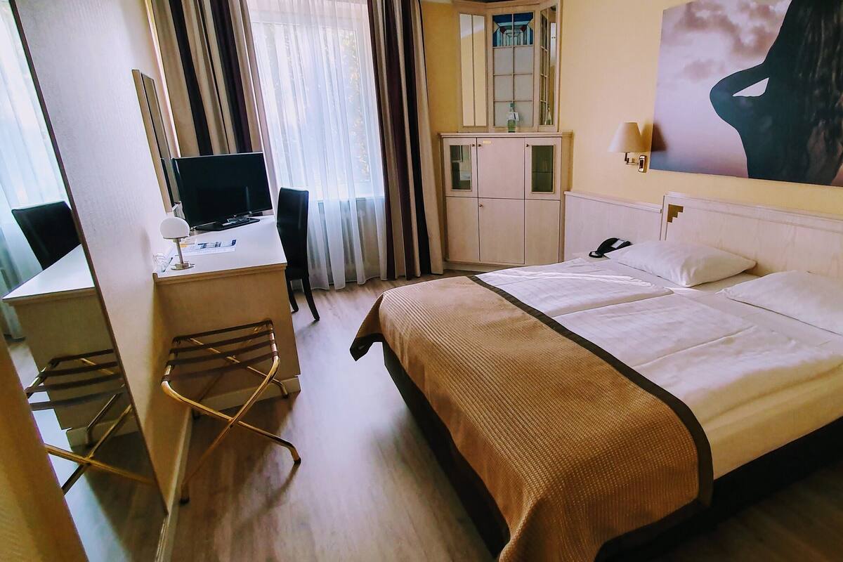 Quarto de hotel com cama, escrivaninha, cadeira e televisão.