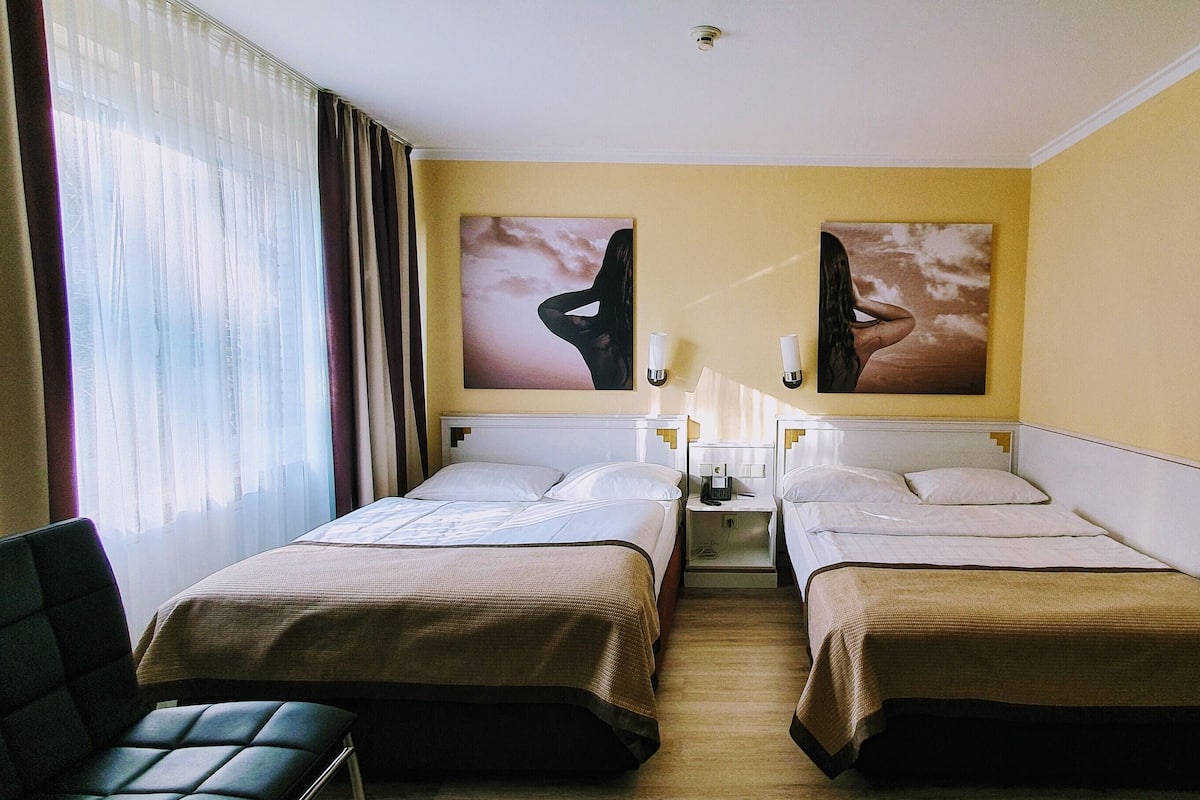 Quarto de hotel com duas camas, uma escrivaninha, uma cadeira e duas luminárias fixadas na parede.