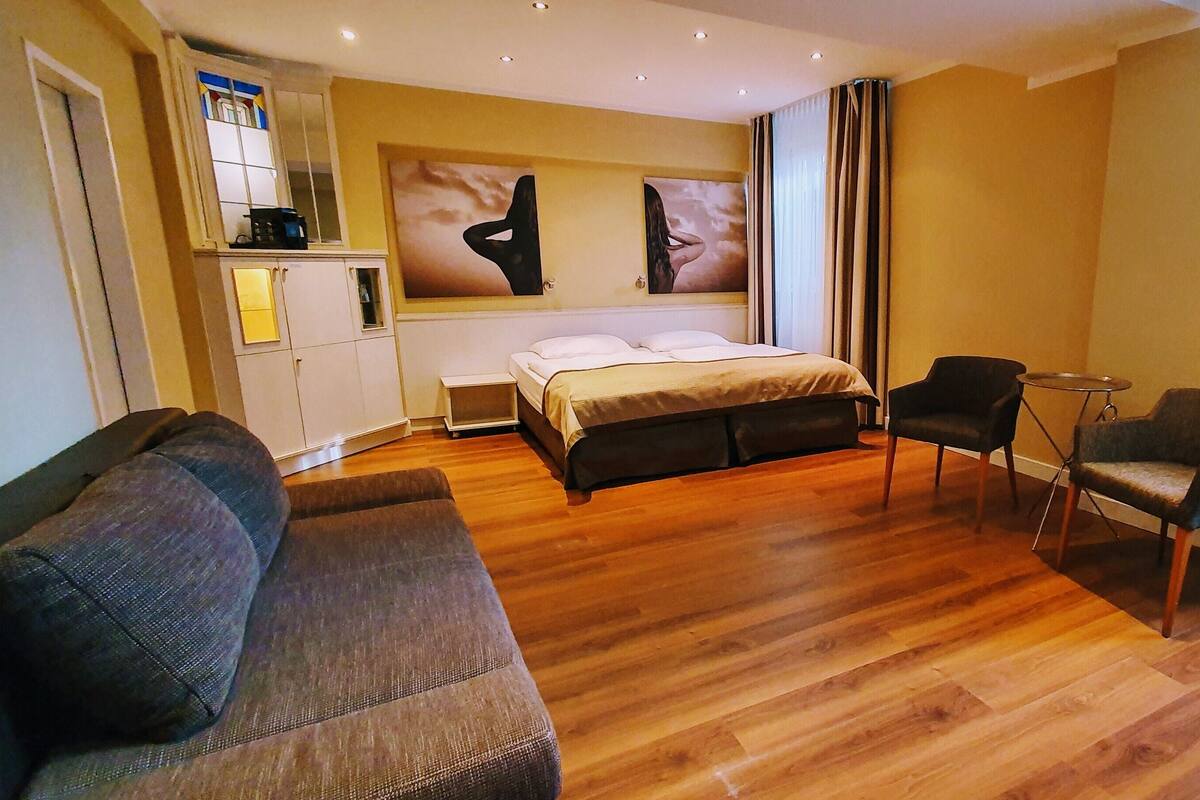 Quarto de hotel com uma cama, duas poltronas, uma mesinha e obras de arte na parede.