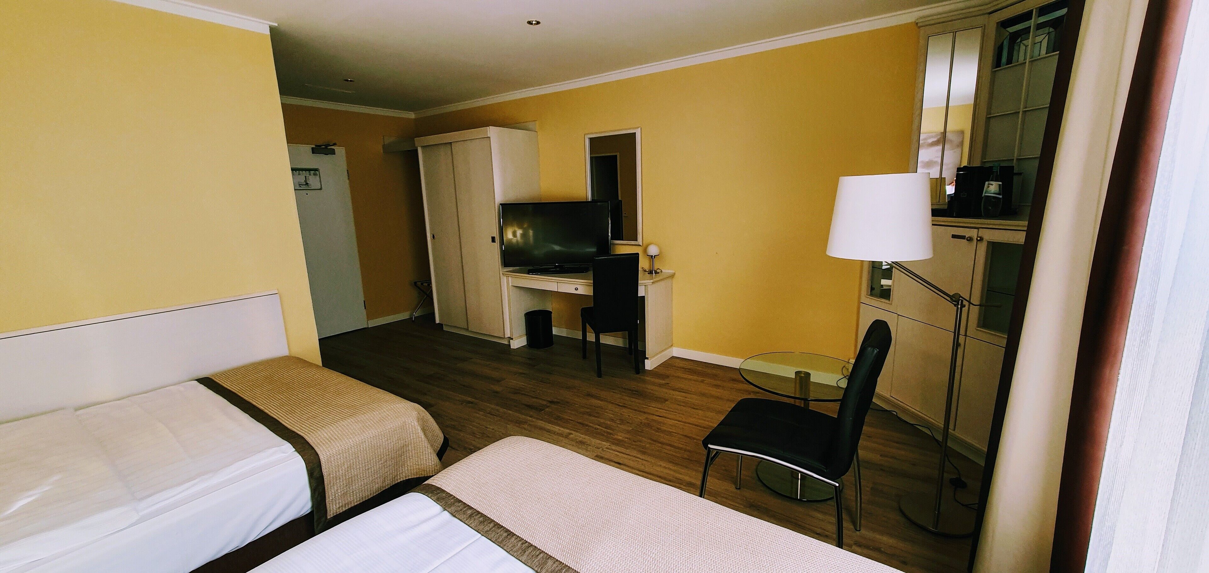 A hotel room with two beds, a desk with a TV, a chair, a lamp, and a small table.