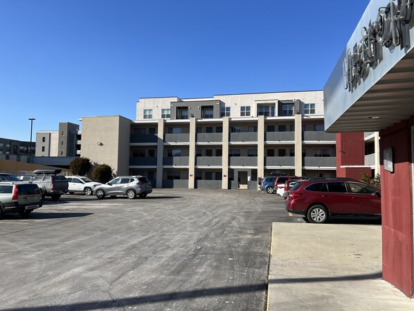 A parking lot with several cars, a multi-story building with balconies, and a sign with the name "Hotel".