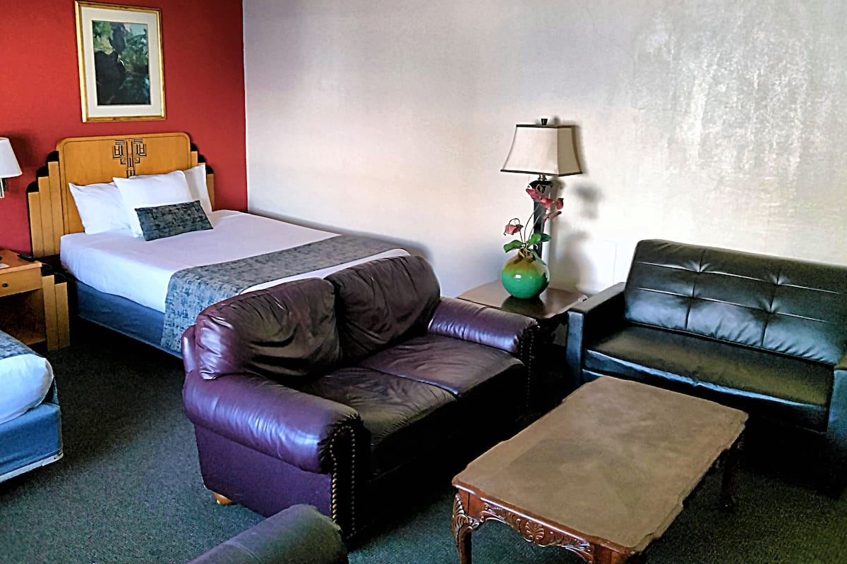 Una habitación de hotel con una cama, dos sofás de cuero, una mesita y una mesita de noche con una lámpara.