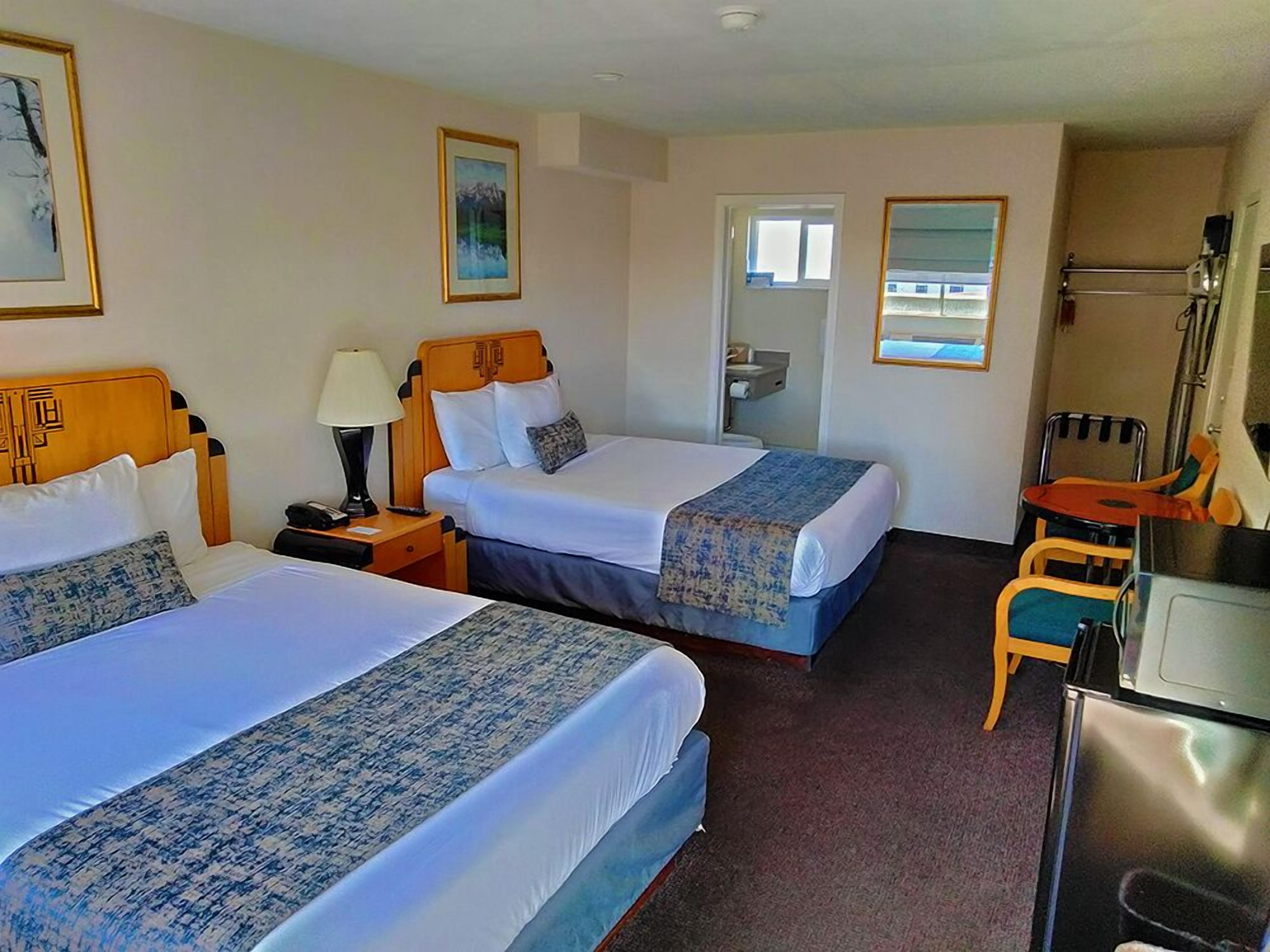 A hotel room with two beds, a desk, a chair, and a small kitchenette.