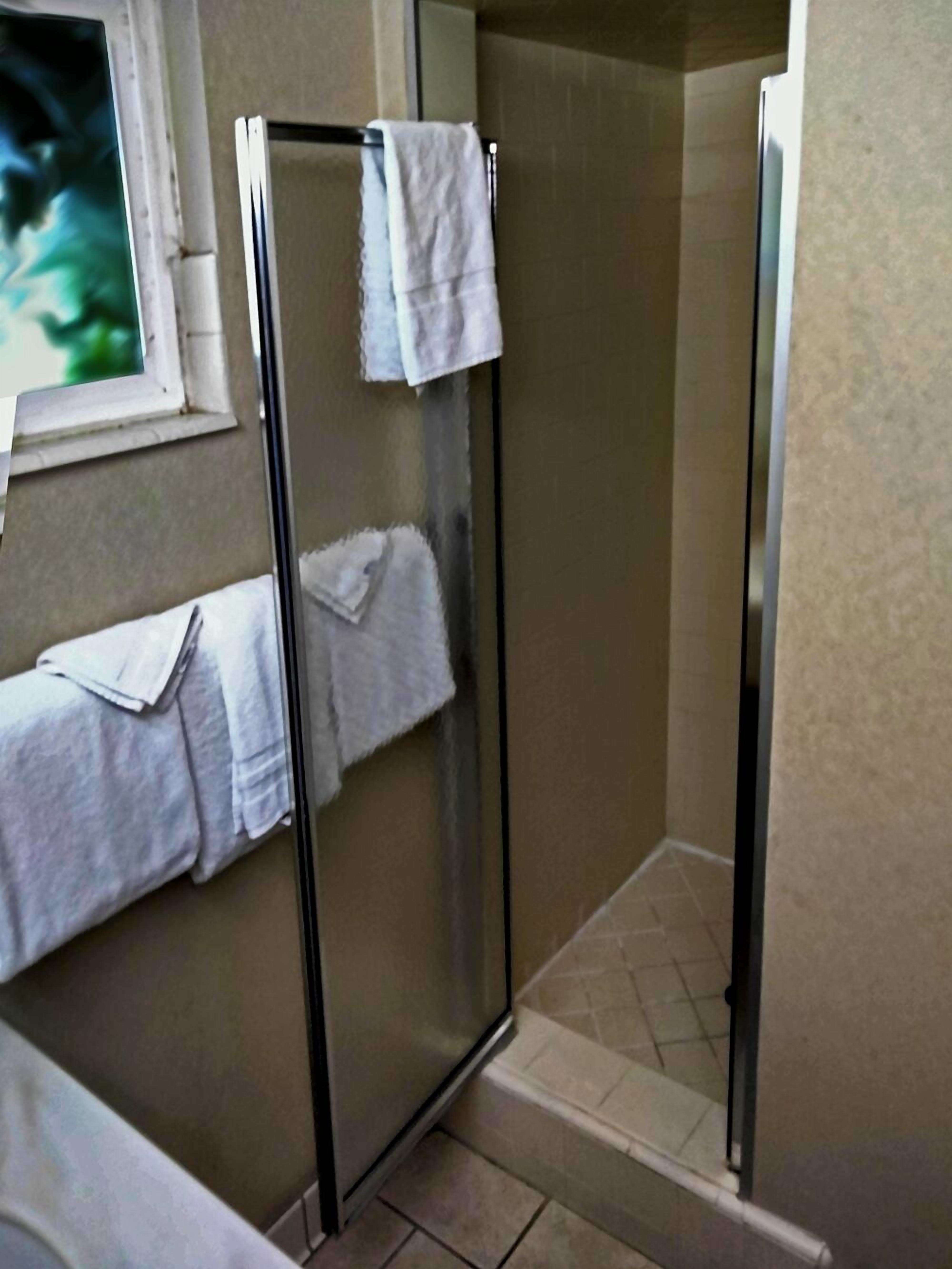Un baño con cabina de ducha de vidrio, perchero y ventana.