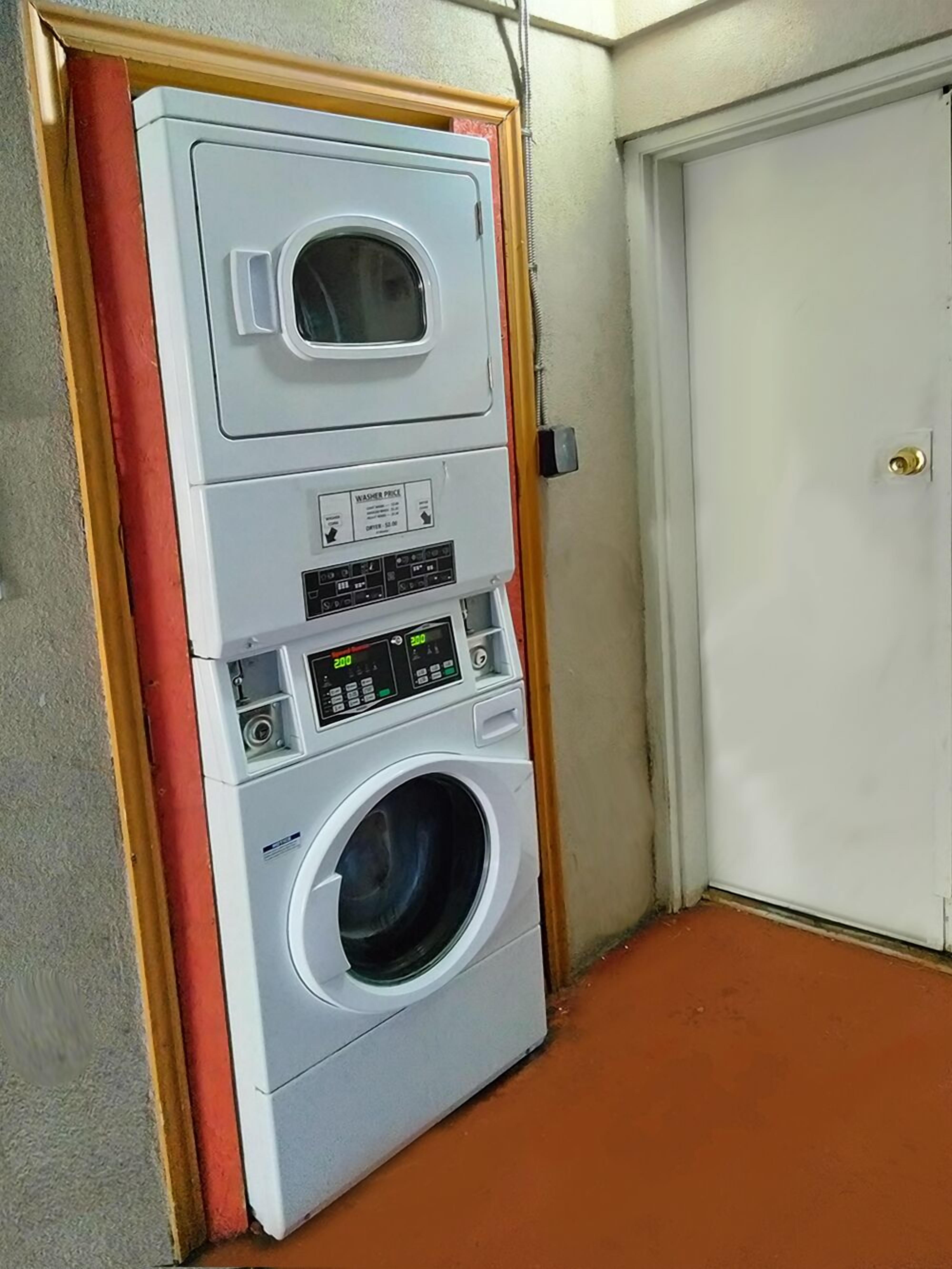 A stacked washer and dryer unit in a room with a closed door and a red floor.