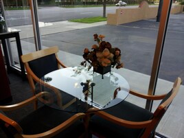 Una mesa de vidrio con sillas, un jarrón de flores y vistas a la calle.