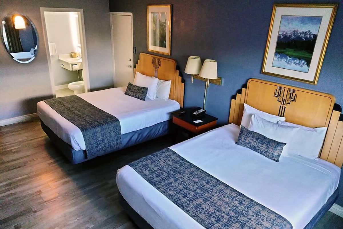 Two double beds with headboards, a bedside table with lamps, a mirror, and a framed picture on the wall.