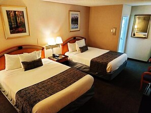 A hotel room with two beds, a nightstand with lamps, and framed pictures on the walls. - The Metropolitan Inn (Salt Lake City)