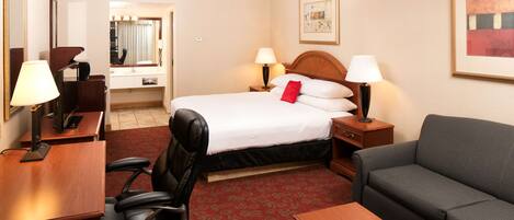 Ein Hotelzimmer mit Bett, Schreibtisch, Stuhl, Sofa und Spiegel.