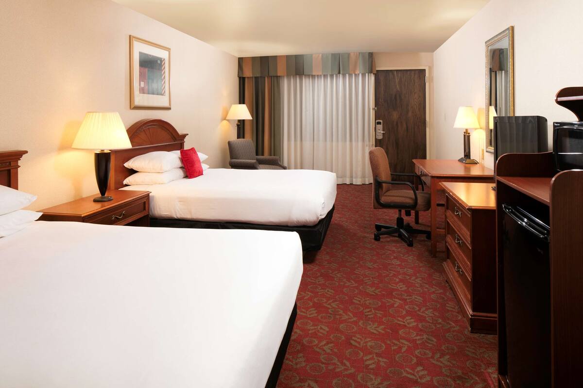 A hotel room with two beds, a desk, a chair, a television, and a mirror.