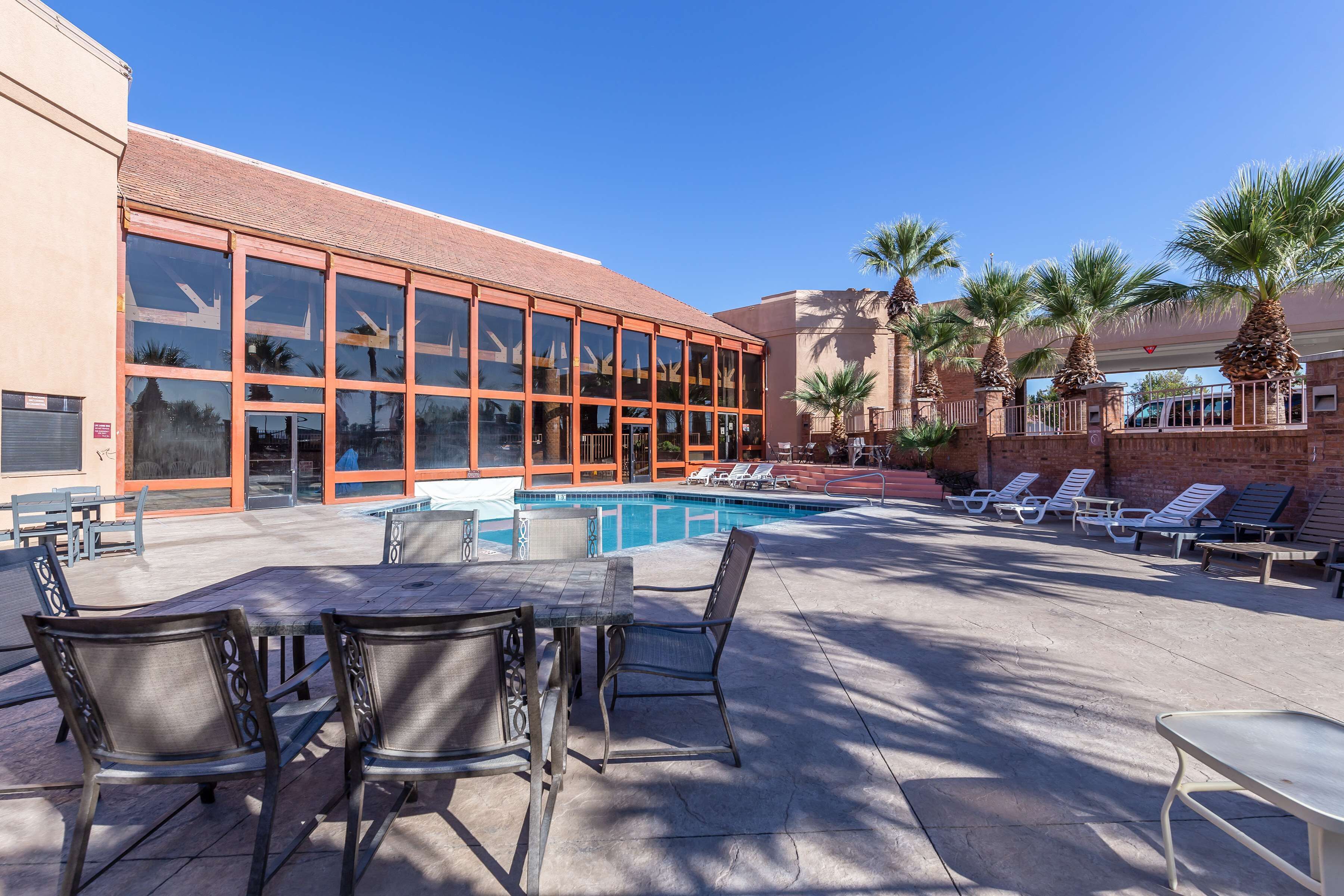 A pool area with lounge chairs and a table, a building with large windows, and palm trees.