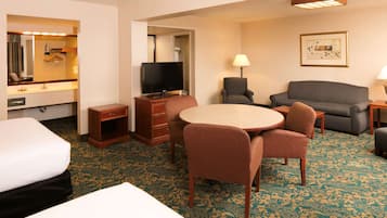 Habitación de hotel con cama, escritorio con televisor, mesa de comedor con sillas, sofá y alfombra estampada.