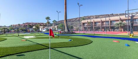 A golf course with a flag, palm trees, and a building in the background.