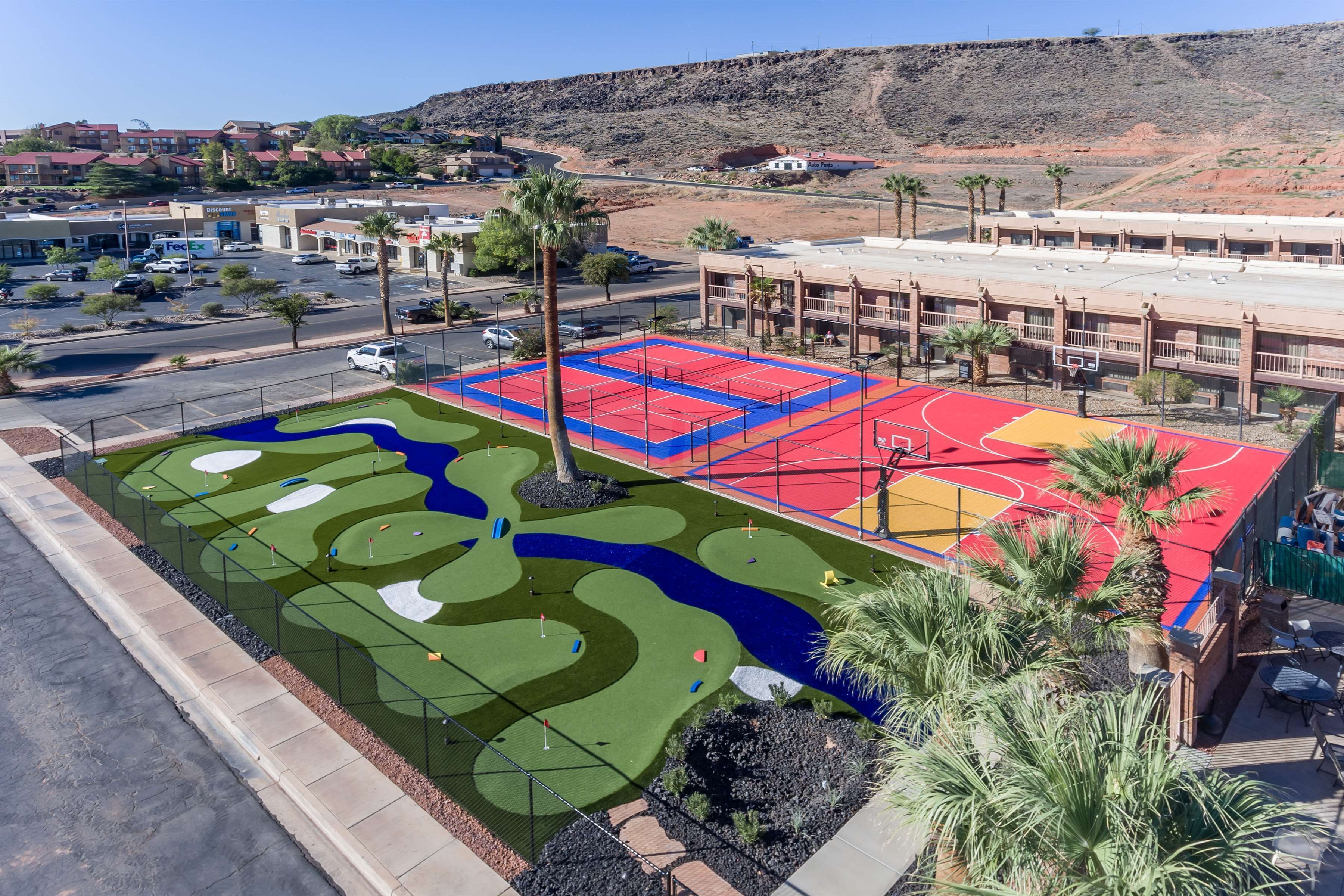 Un campo de golf con zonas de juego en rojo y verde, rodeado por un estacionamiento y edificios.