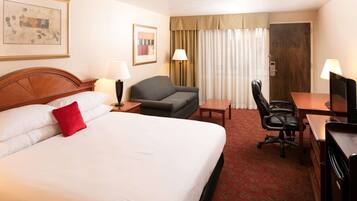 A hotel room with a large bed, a desk, a chair, and a sofa.