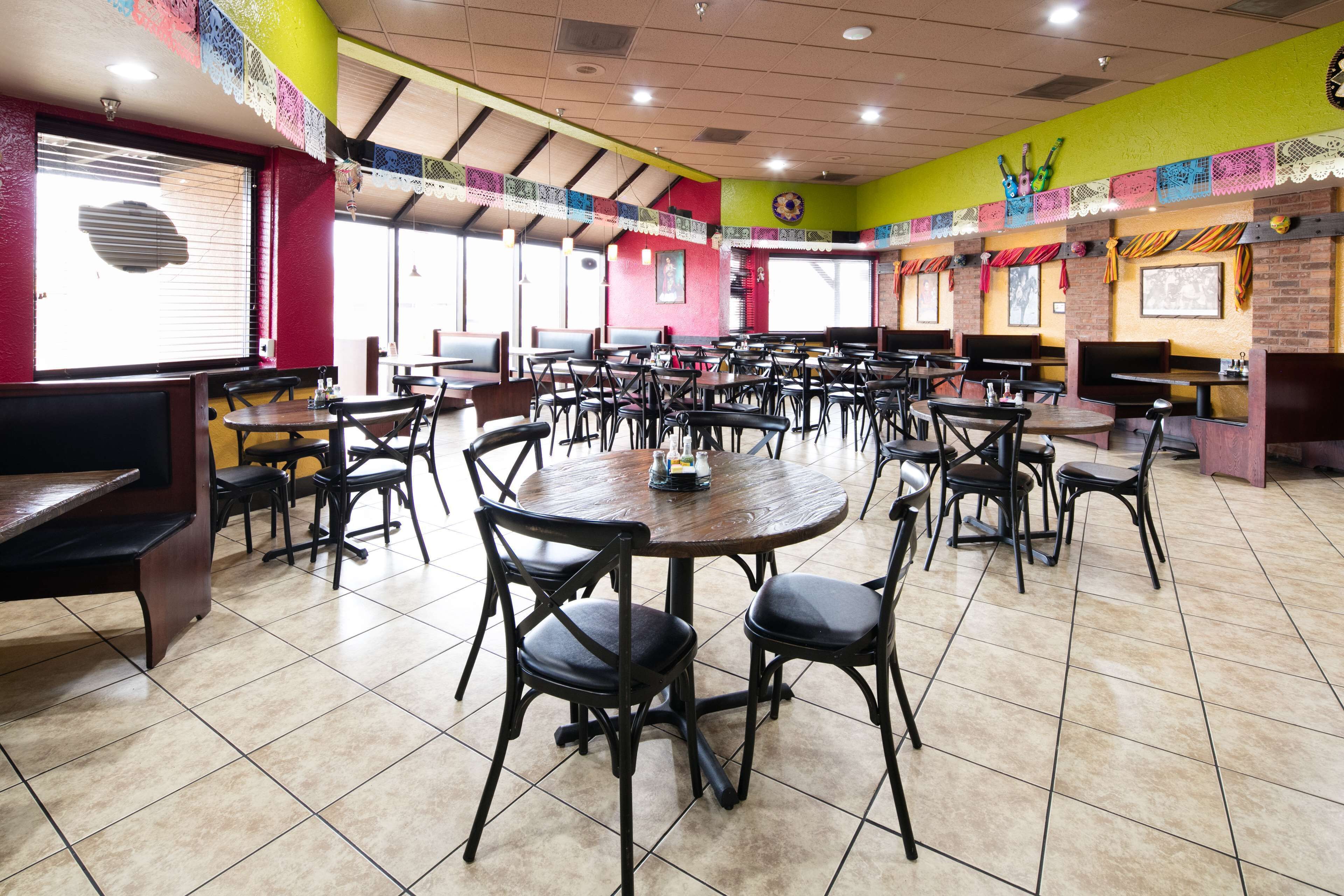 A spacious restaurant with multiple tables and chairs, large windows, and colorful decorations.
