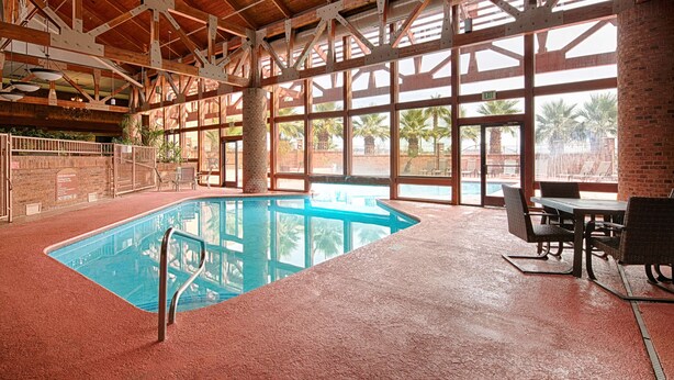 An indoor swimming pool with a view of palm trees outside, surrounded by wooden beams and large windows. - Red Lion Hotel & Conference Center St. George, UT (St. George)