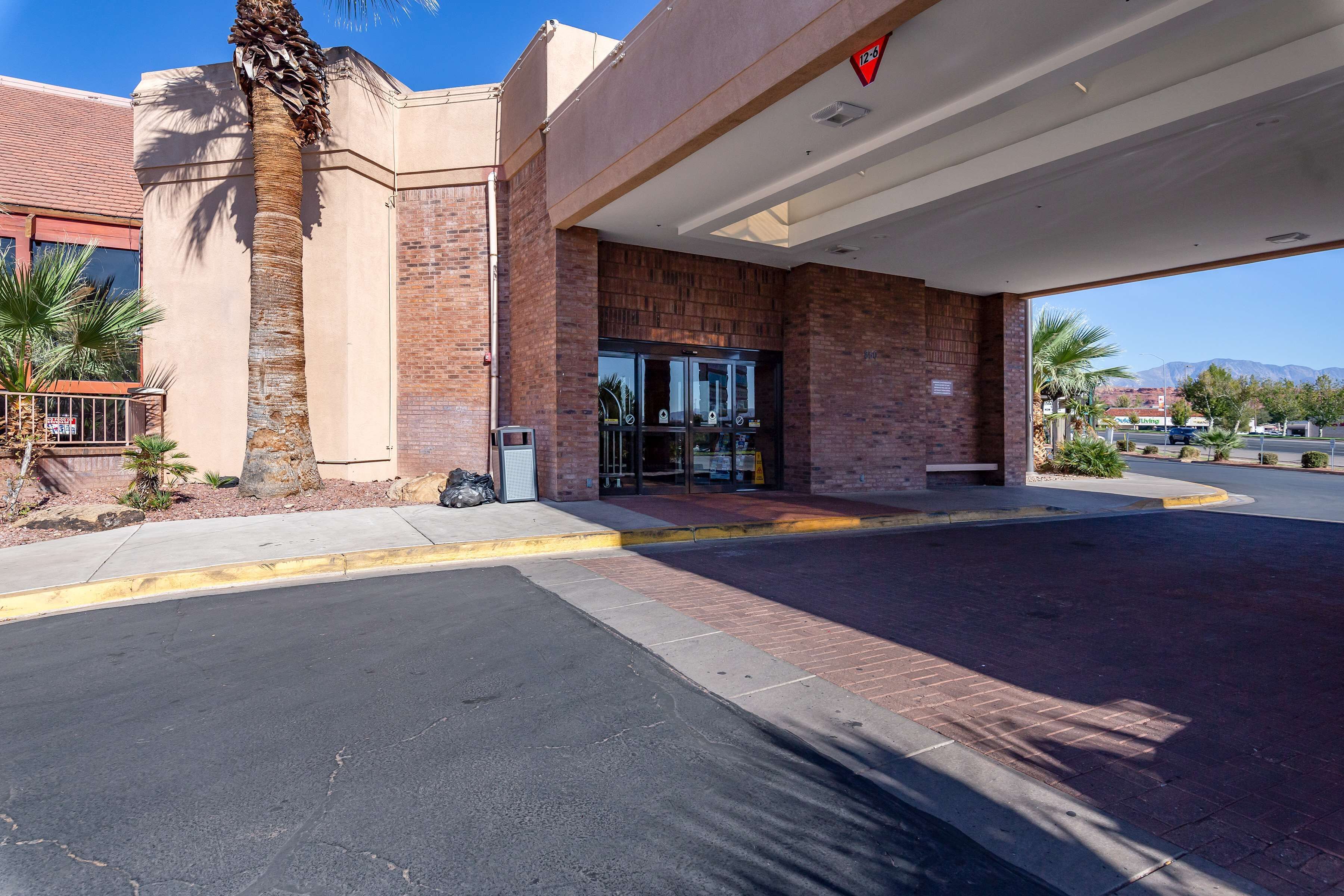A hotel entrance with a brick facade, palm trees, and a clear sky.