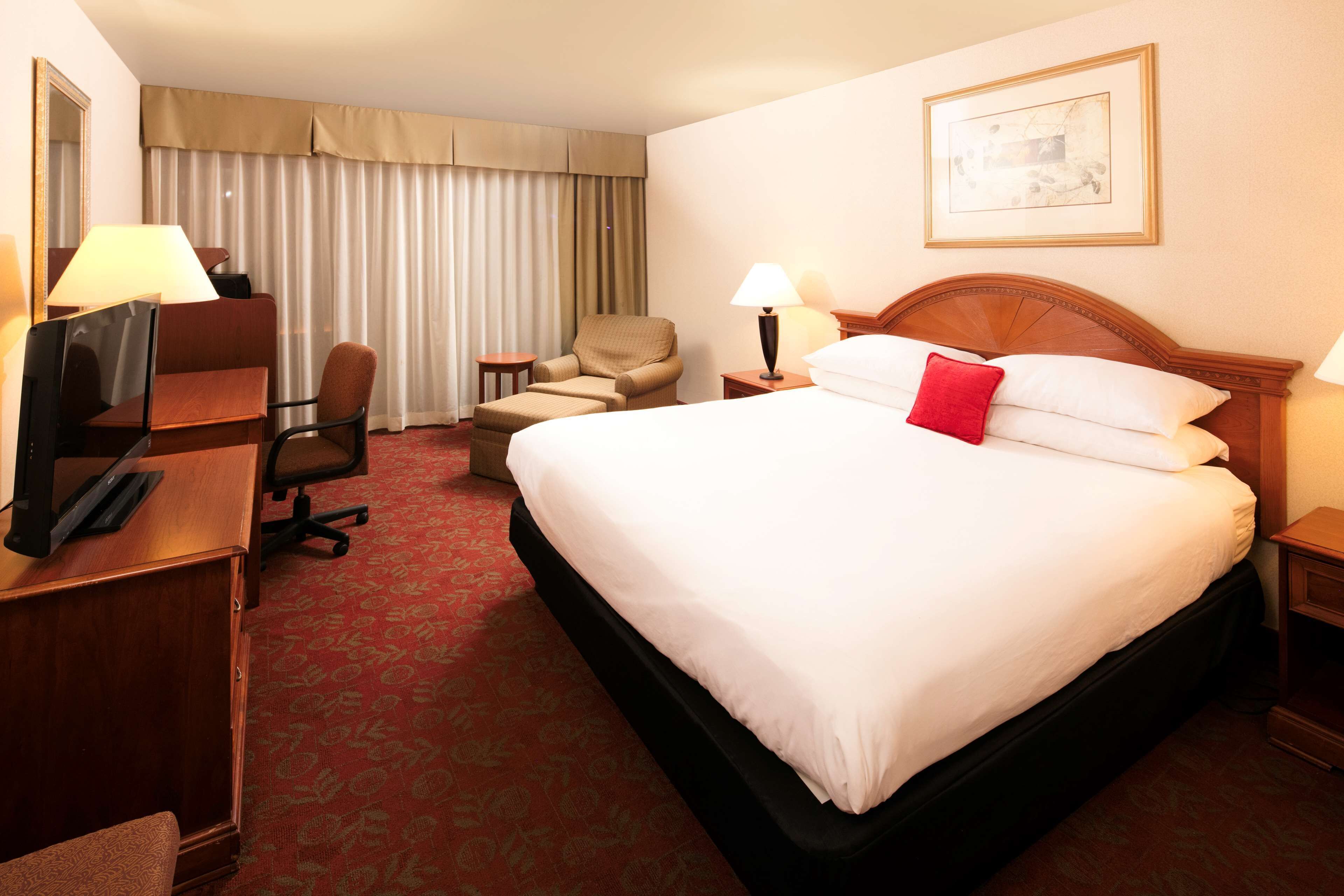 A hotel room with a large bed, a desk with a computer, a chair, a small table, and a lamp.