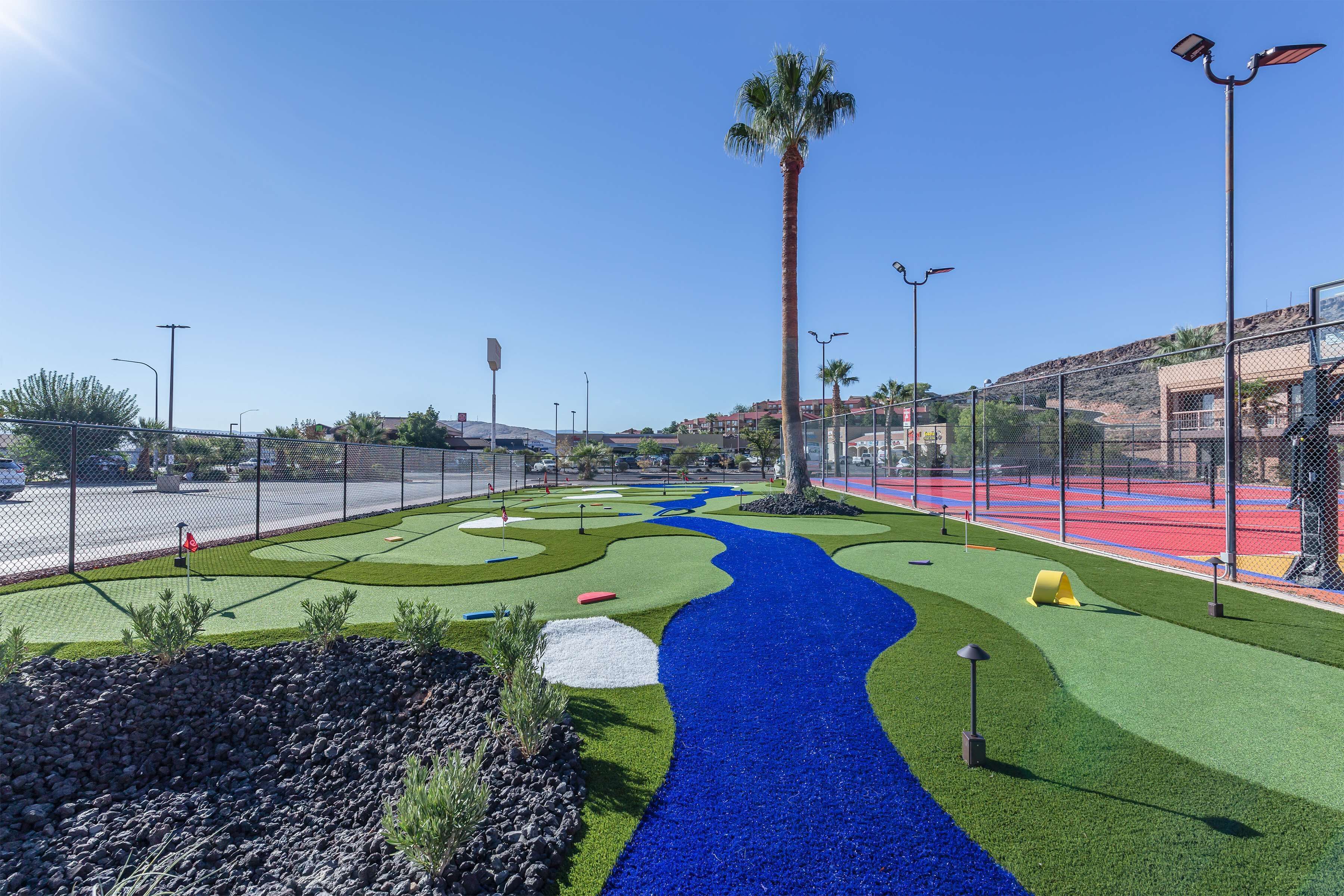 En golfbana med en blå vattenanläggning, palmer och ett inhägnat område med sportplaner.