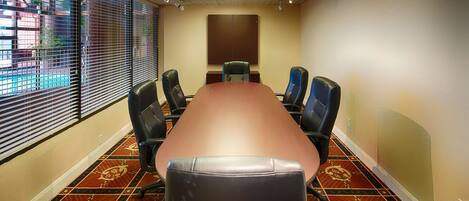 A conference room with a long table, six chairs, and patterned carpet.