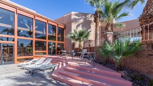 A building with large glass windows, outdoor seating, palm trees, and a stone wall. - Red Lion Hotel & Conference Center St. George, UT (St. George)