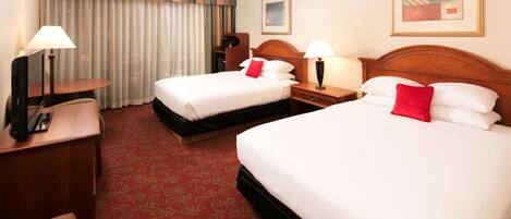 A hotel room with two beds, a desk, a chair, a lamp, and a large window with curtains.