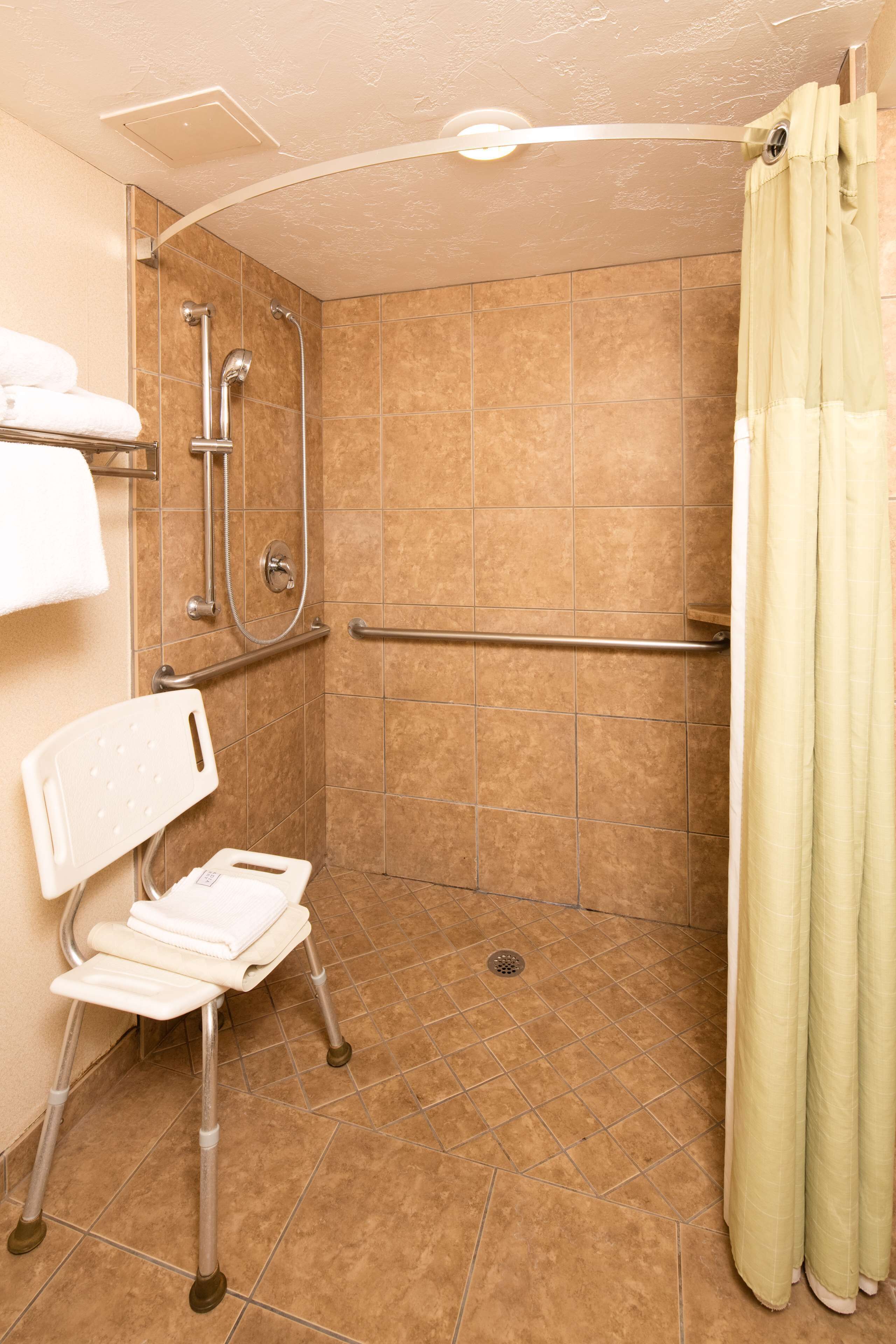 A bathroom with a shower, grab bars, a wheelchair-accessible bench, and a curtain.