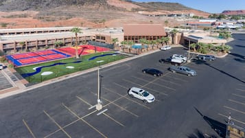 A parking lot with several cars, a sports court, and a building with multiple floors and a flat roof.