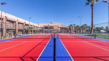 Una cancha de tenis con una red, rodeada por una cerca, y un edificio al fondo.