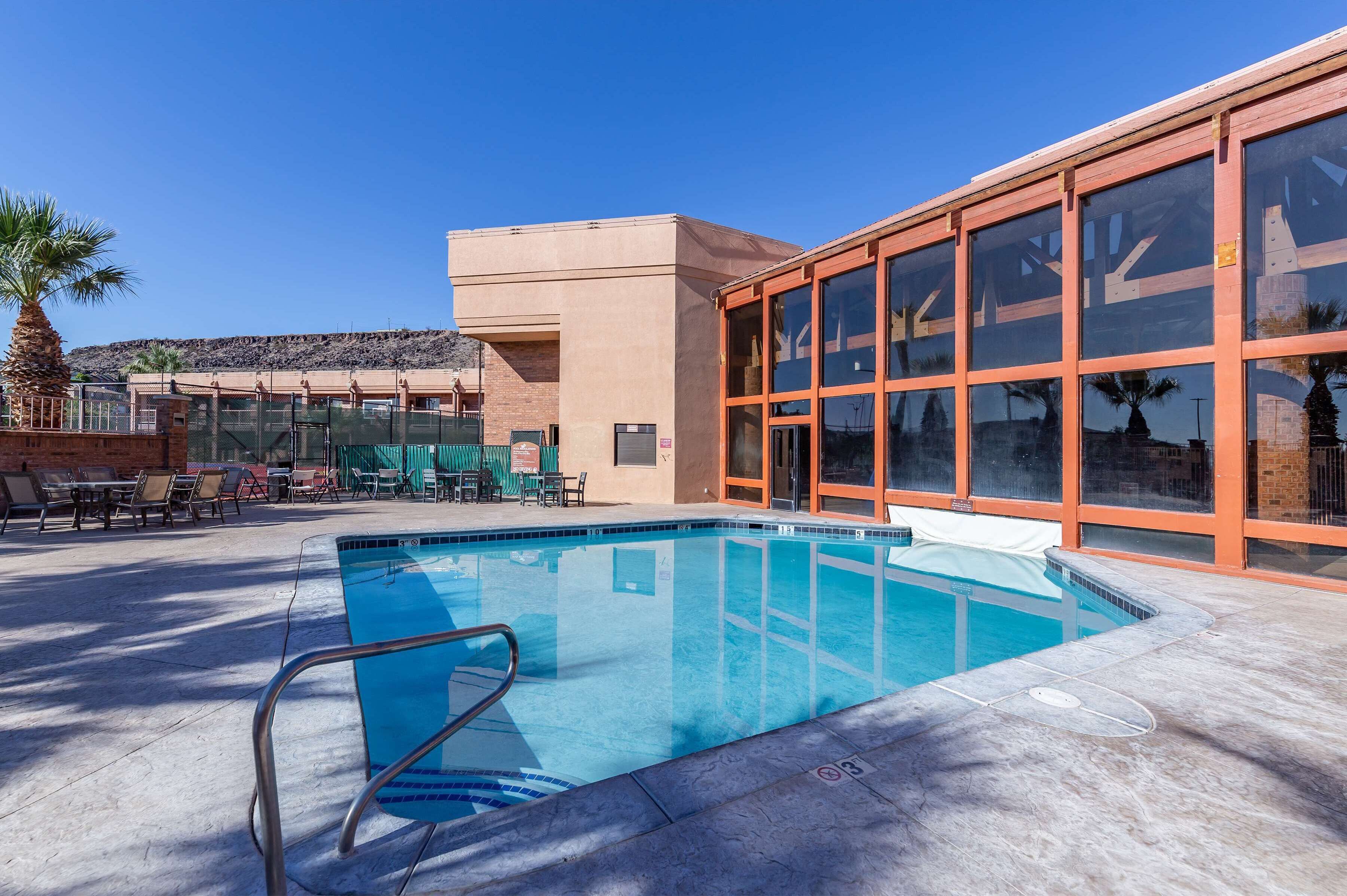 Una piscina con agua cristalina azul, rodeada de sillas de descanso y un edificio con ventanas amplias.