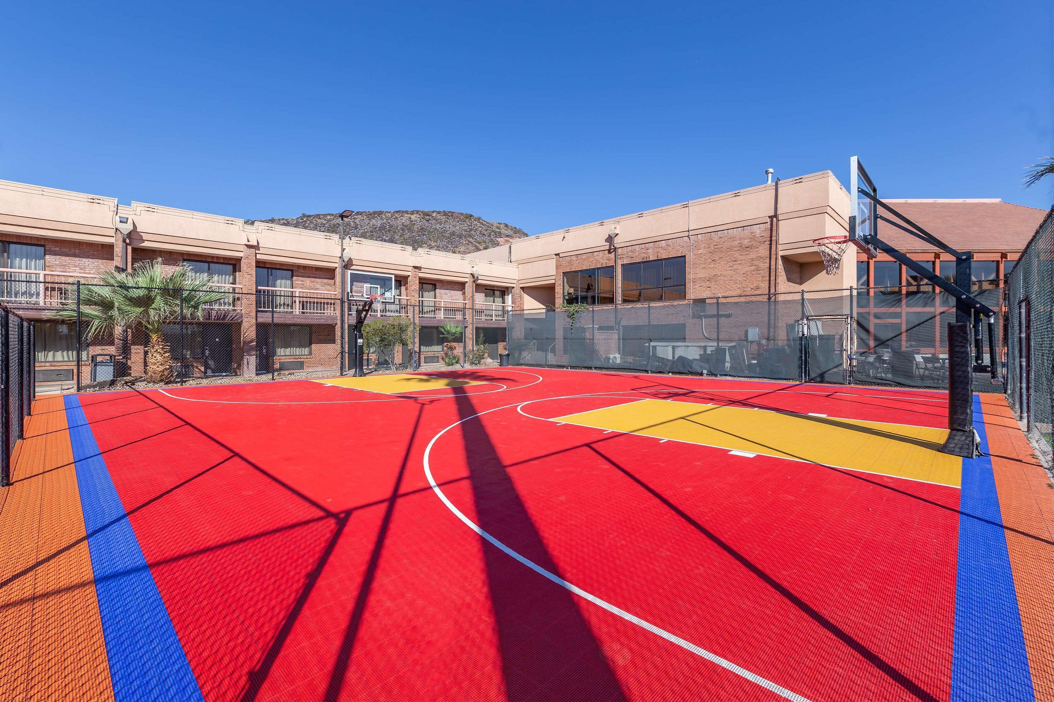 An indoor basketball court with red and yellow markings, surrounded by a building with multiple windows and balconies.