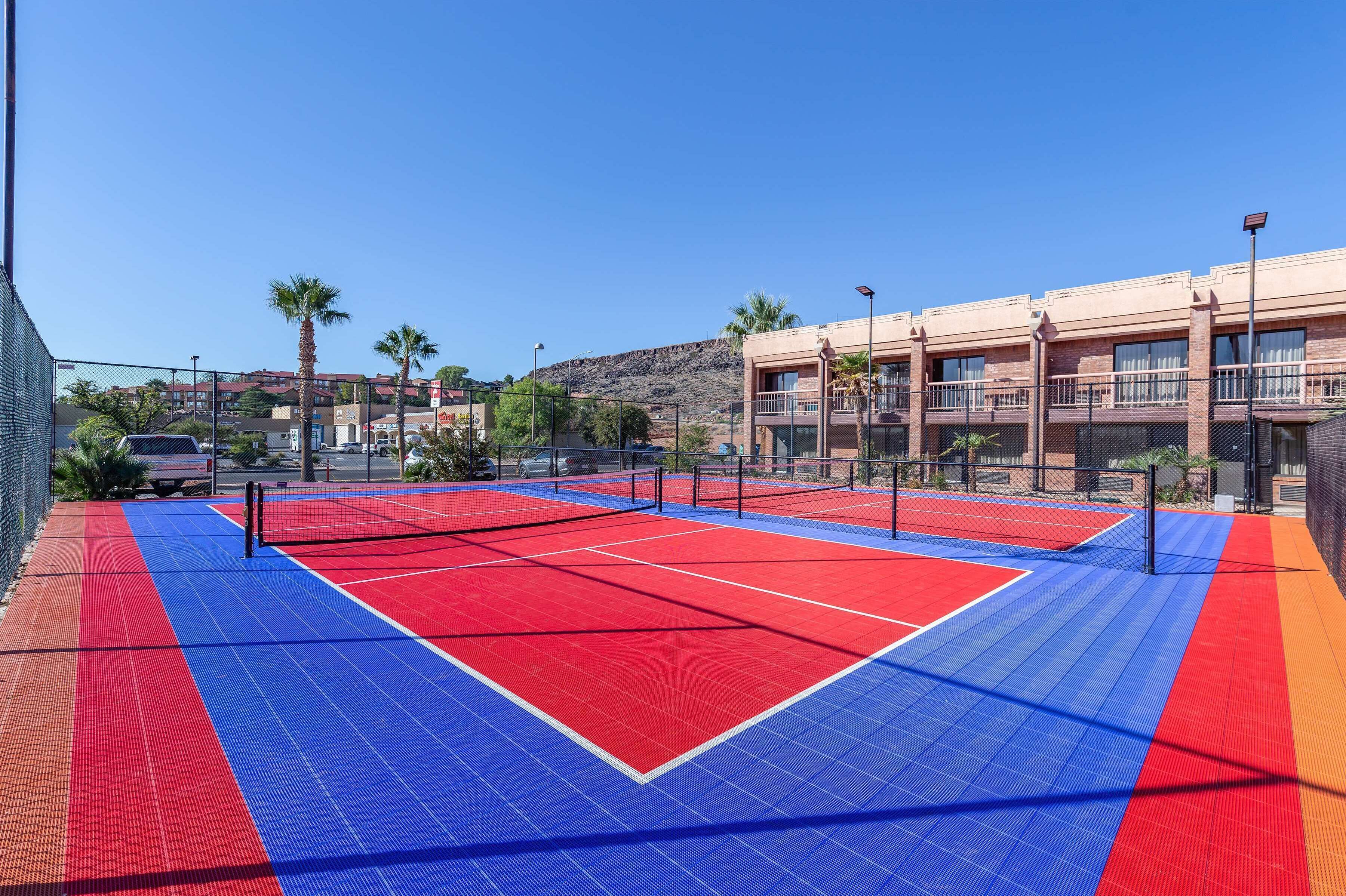 Een tennisbaan met een net, omringd door een hek, naast een gebouw met balkons.