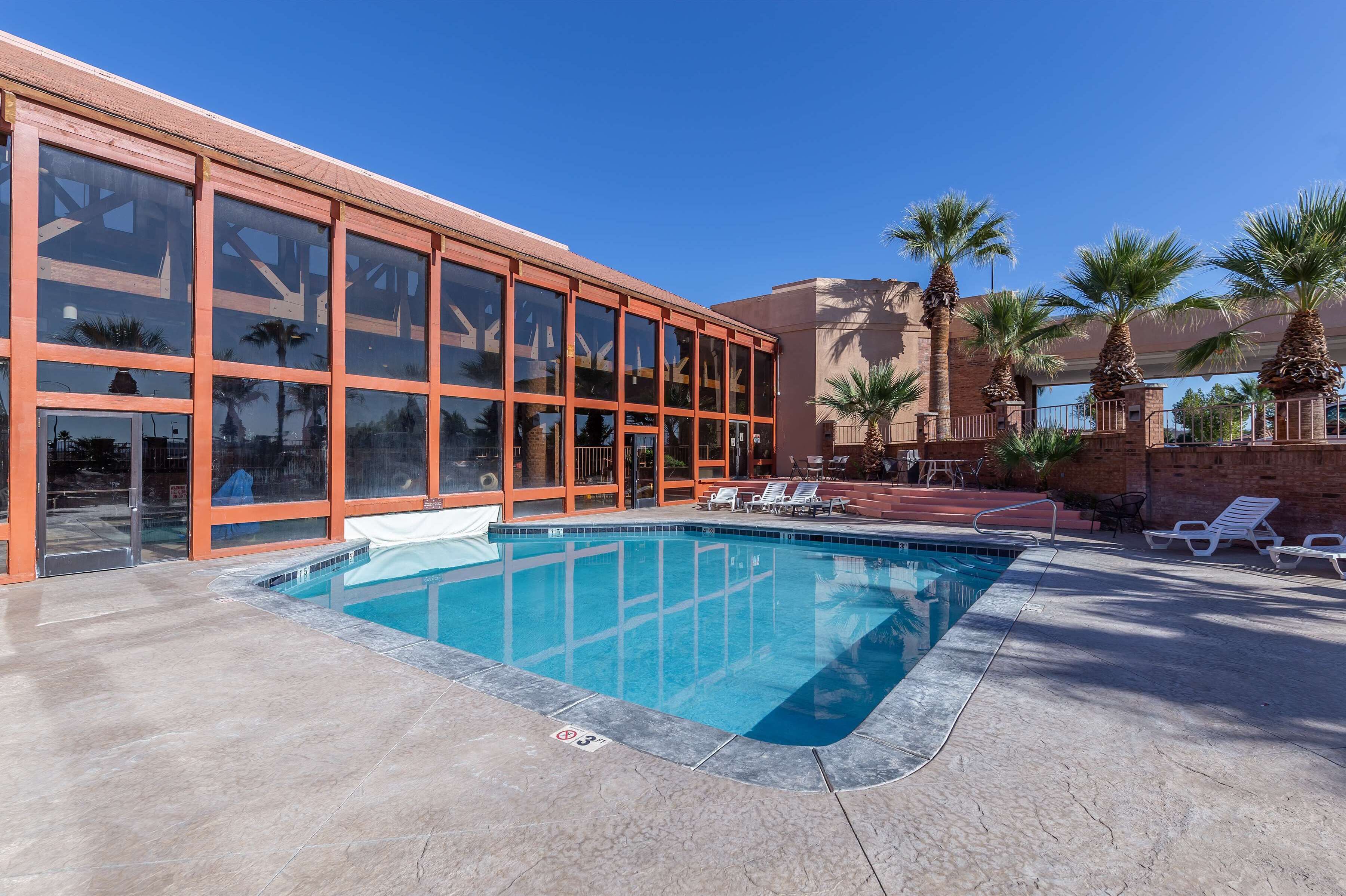 A swimming pool with lounge chairs and palm trees, surrounded by a building with large windows and a brick facade.