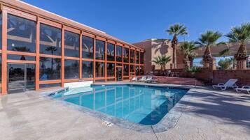 A swimming pool with lounge chairs and palm trees, surrounded by a building with large windows and a brick facade.