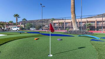 Un campo de mini golf con una bandera roja, palmeras y un edificio al fondo.