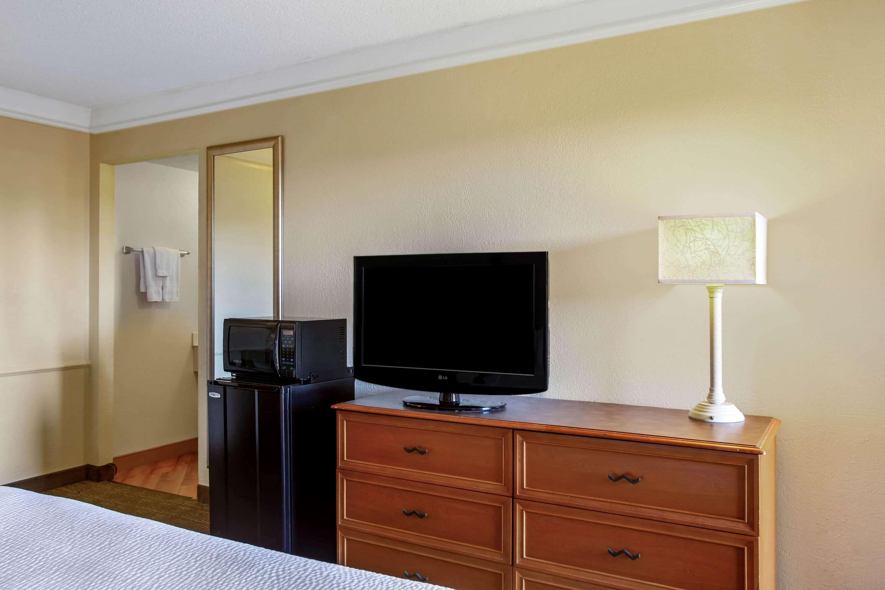 A hotel room with a bed, a wooden dresser, a television, a microwave, and a lamp.