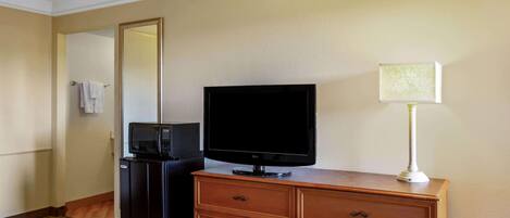 Una habitación de hotel con una cama, un aparador de madera, un televisor, un microondas y una lámpara.
